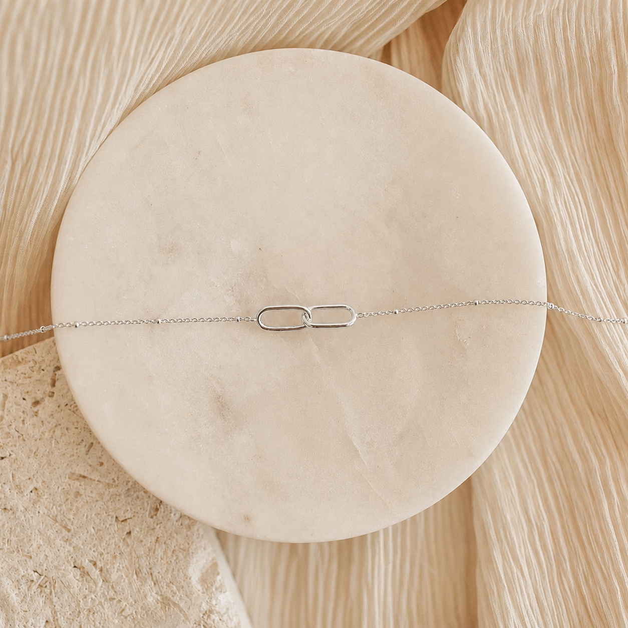 Silver bracelet on a round beige stone with a natural wood background